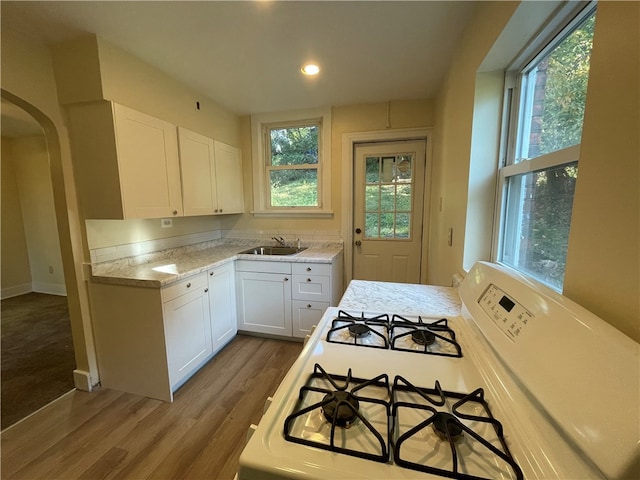 kitchen featuring light stone counters, white cabinets, sink, white gas range oven, and light hardwood / wood-style floors