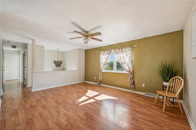 empty room with ceiling fan with notable chandelier and hardwood / wood-style flooring