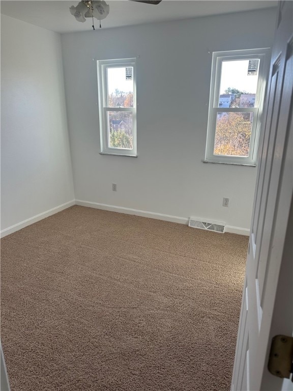 carpeted spare room featuring a wealth of natural light and ceiling fan