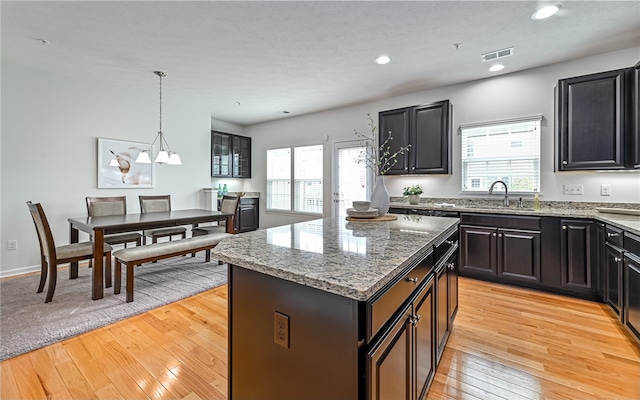 kitchen featuring light wood-type flooring, pendant lighting, stone counters, and a center island