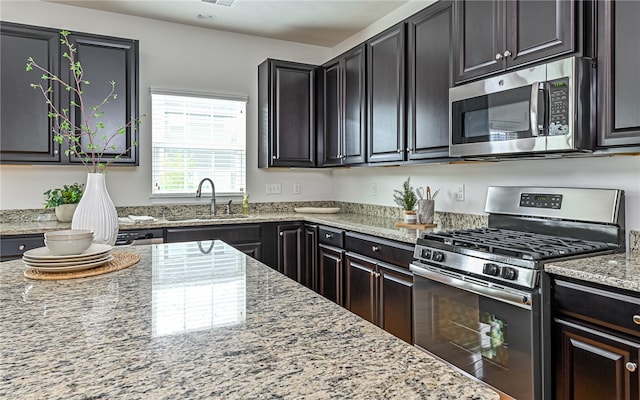 kitchen with appliances with stainless steel finishes, sink, and light stone counters