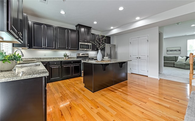 kitchen with appliances with stainless steel finishes, a kitchen island, a breakfast bar area, and light hardwood / wood-style flooring