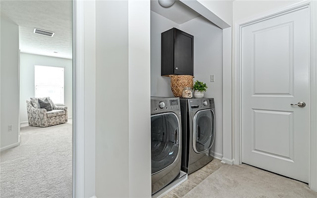 laundry room with a textured ceiling, light colored carpet, washing machine and clothes dryer, and cabinets