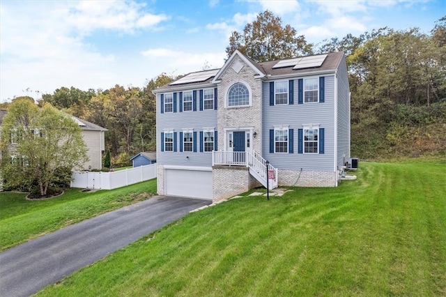 colonial home with a garage, a front lawn, and solar panels