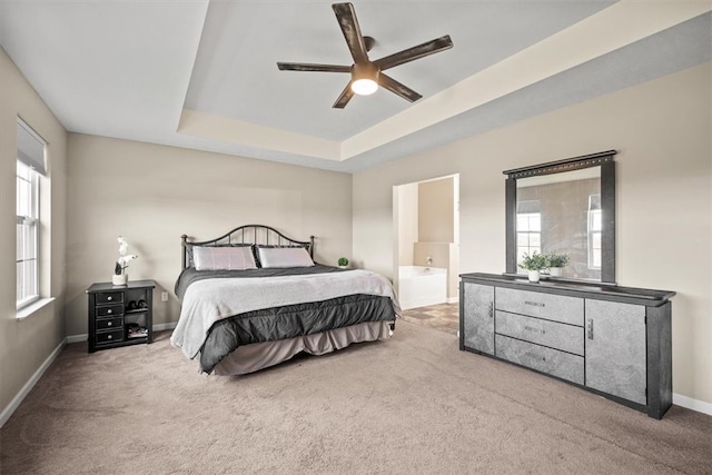 carpeted bedroom featuring ceiling fan, a tray ceiling, and ensuite bath