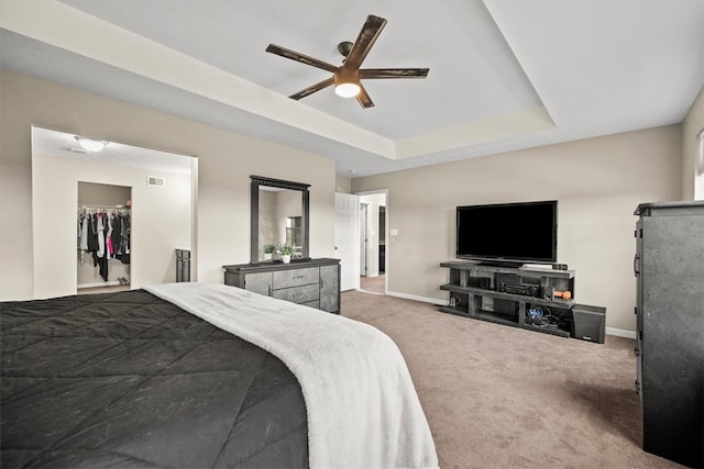 carpeted bedroom with a spacious closet, a tray ceiling, a closet, and ceiling fan