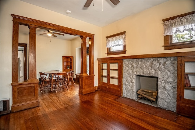 living room with ceiling fan, a stone fireplace, decorative columns, and wood-type flooring