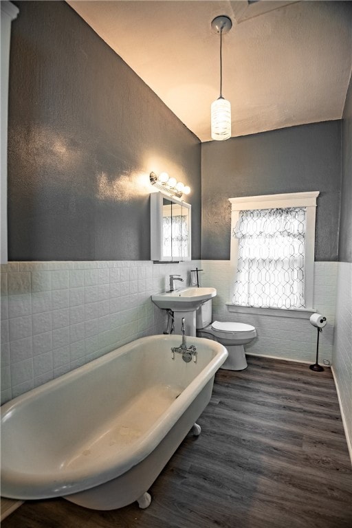 bathroom featuring tile walls, wood-type flooring, toilet, and a washtub