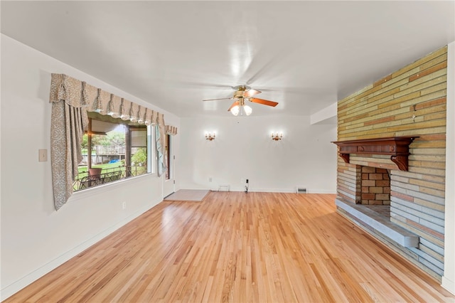 unfurnished living room featuring ceiling fan, wood-type flooring, and a brick fireplace