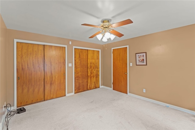 unfurnished bedroom featuring ceiling fan, light carpet, and multiple closets