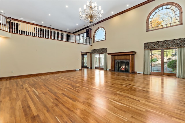 unfurnished living room featuring a towering ceiling, ornamental molding, a chandelier, and light wood-type flooring