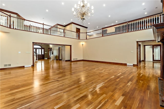 unfurnished living room with an inviting chandelier, crown molding, a high ceiling, and light wood-type flooring