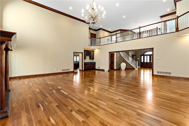 unfurnished living room featuring a towering ceiling, crown molding, hardwood / wood-style flooring, and an inviting chandelier