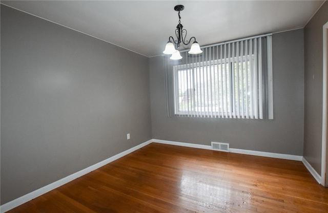 spare room with a notable chandelier and wood-type flooring