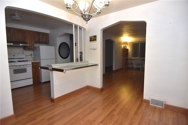 kitchen featuring dark hardwood / wood-style flooring, backsplash, a breakfast bar, white appliances, and exhaust hood