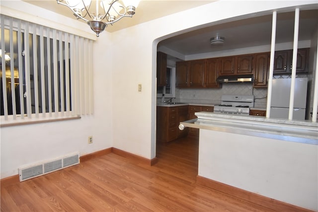 kitchen featuring light hardwood / wood-style flooring, stainless steel fridge, white gas range, tasteful backsplash, and a notable chandelier