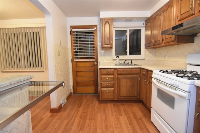 kitchen with sink, white range with gas stovetop, ventilation hood, backsplash, and light hardwood / wood-style floors