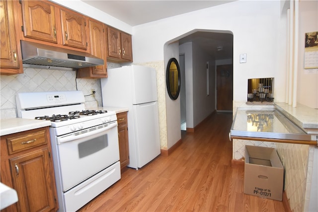 kitchen with tasteful backsplash, white appliances, range hood, and light hardwood / wood-style flooring