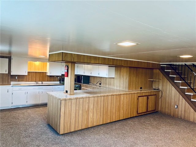 kitchen featuring white cabinetry, carpet, and wooden walls