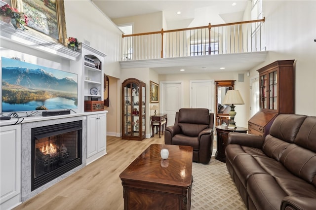 living room featuring light hardwood / wood-style floors, built in features, a towering ceiling, and plenty of natural light