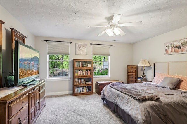 bedroom with ceiling fan, light carpet, and a textured ceiling