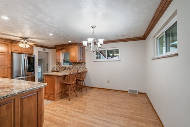 kitchen featuring a kitchen bar, hanging light fixtures, stainless steel fridge, a wealth of natural light, and light hardwood / wood-style flooring