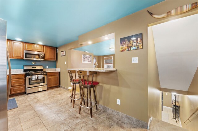 kitchen with a breakfast bar area, light tile patterned flooring, kitchen peninsula, and stainless steel appliances