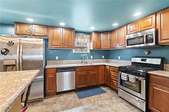 kitchen featuring light stone counters, stainless steel appliances, and sink