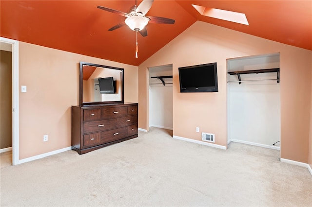 unfurnished bedroom featuring vaulted ceiling with skylight, light carpet, and ceiling fan