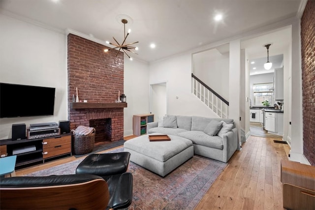 living room with light hardwood / wood-style floors, ornamental molding, a chandelier, and a brick fireplace