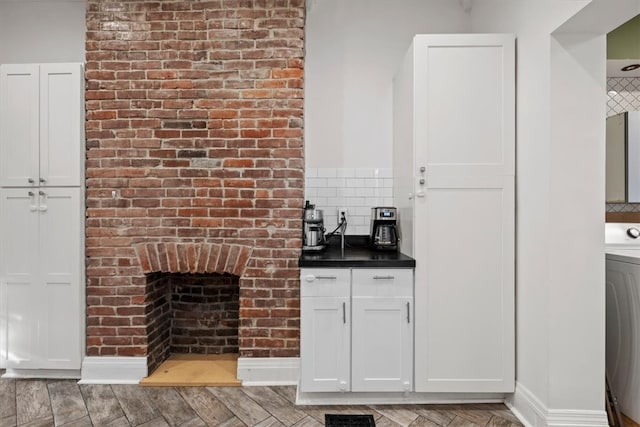 bar featuring washer / dryer, decorative backsplash, white cabinets, light hardwood / wood-style flooring, and a fireplace