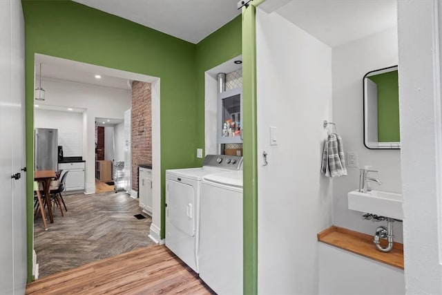 clothes washing area with sink, washer and dryer, and light parquet flooring