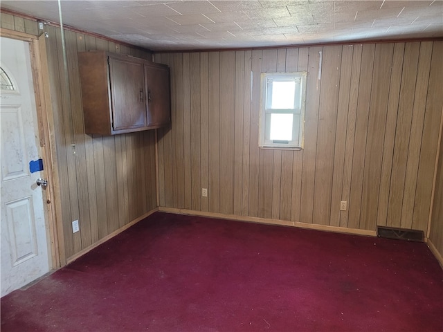 unfurnished room featuring wooden walls and dark colored carpet