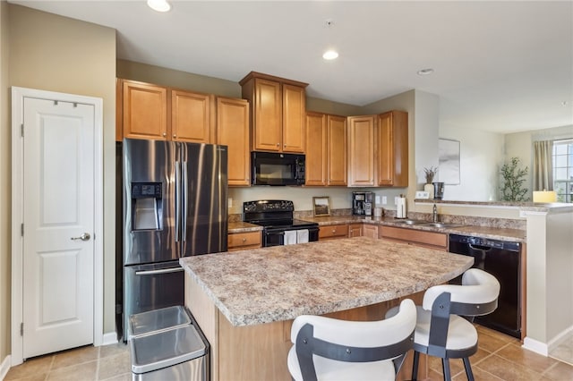 kitchen with light stone countertops, sink, black appliances, a kitchen island, and a breakfast bar