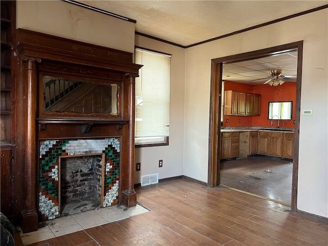 living room featuring ceiling fan, a textured ceiling, ornamental molding, a fireplace, and light hardwood / wood-style floors