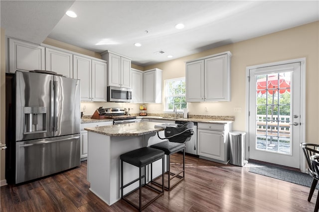 kitchen featuring dark hardwood / wood-style floors, a center island, a kitchen bar, white cabinets, and appliances with stainless steel finishes