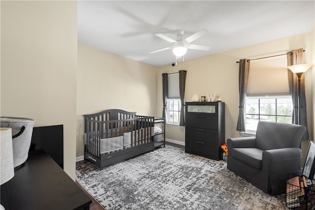 bedroom with multiple windows, a nursery area, and ceiling fan