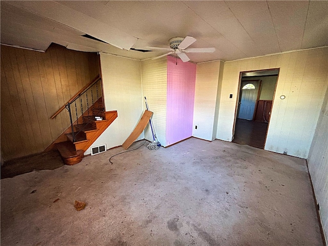 interior space with ceiling fan, wooden walls, and concrete flooring