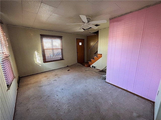 carpeted empty room featuring wooden walls and ceiling fan