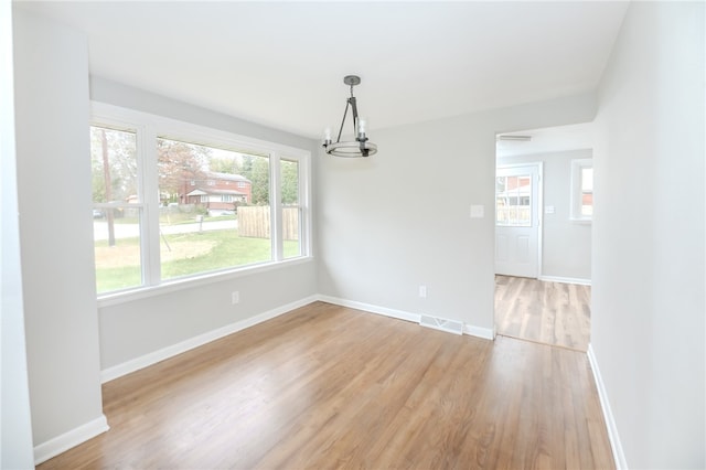 unfurnished dining area featuring an inviting chandelier and light wood-type flooring