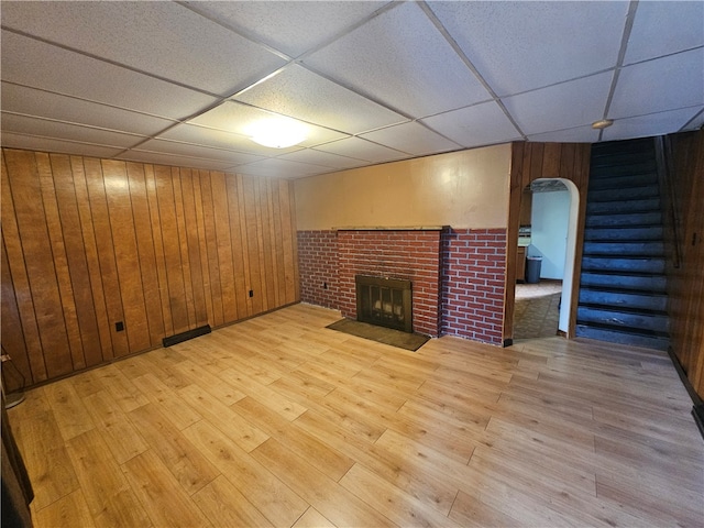 unfurnished living room featuring a fireplace, a paneled ceiling, light wood-type flooring, and wood walls