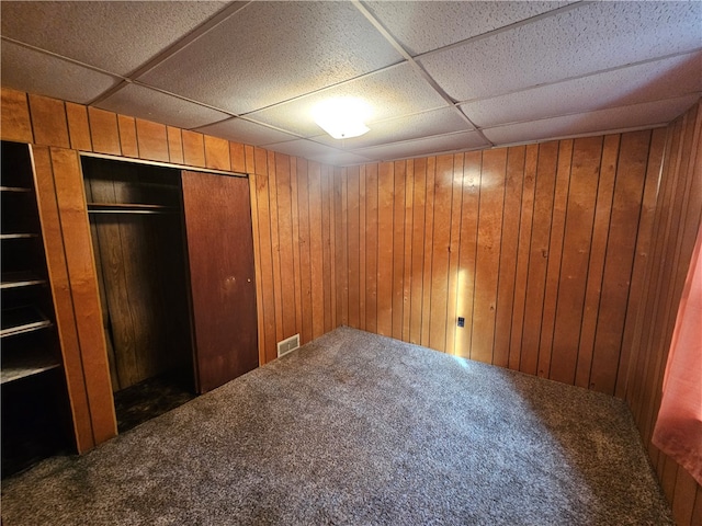 basement featuring wood walls, a drop ceiling, and dark carpet