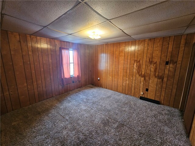 carpeted empty room with a paneled ceiling and wood walls