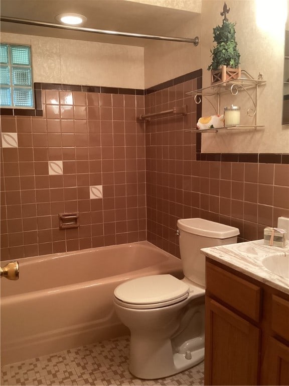 full bathroom featuring toilet, tile patterned floors, tile walls, vanity, and tiled shower / bath combo