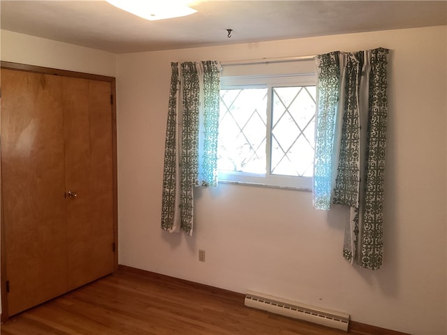 unfurnished bedroom with a closet, a baseboard heating unit, and hardwood / wood-style floors