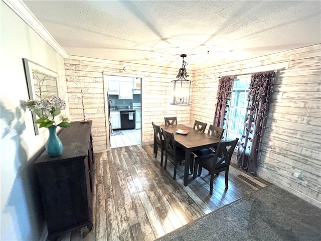 dining room featuring an inviting chandelier, a textured ceiling, wooden walls, and dark wood-type flooring