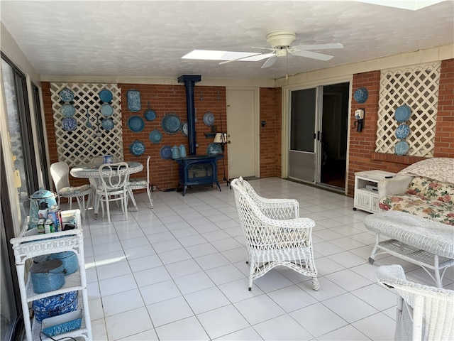 tiled living room with ceiling fan, brick wall, and a wood stove