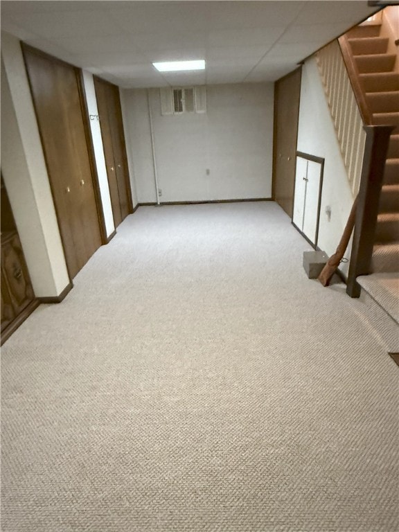 basement featuring a drop ceiling and light colored carpet