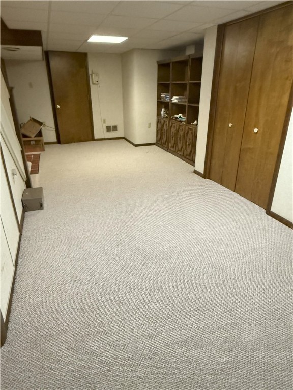 basement with a drop ceiling and light carpet