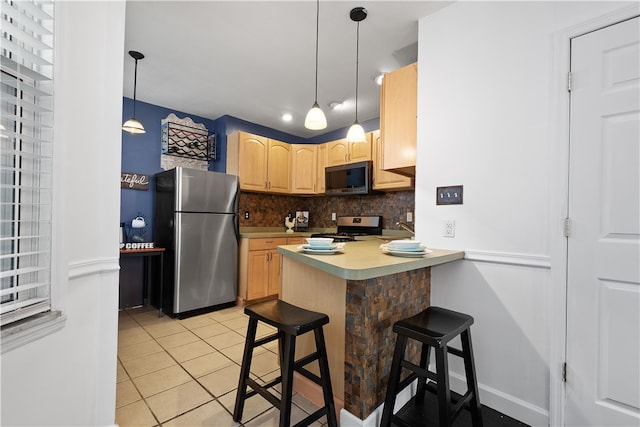 kitchen with kitchen peninsula, appliances with stainless steel finishes, light brown cabinetry, backsplash, and a breakfast bar area